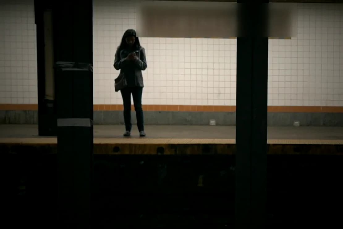 A woman waiting alone on a tiled subway platform, in plain natural colour.