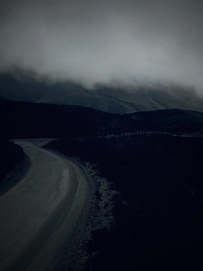 An empty mountain road curving away beneath low cloud.