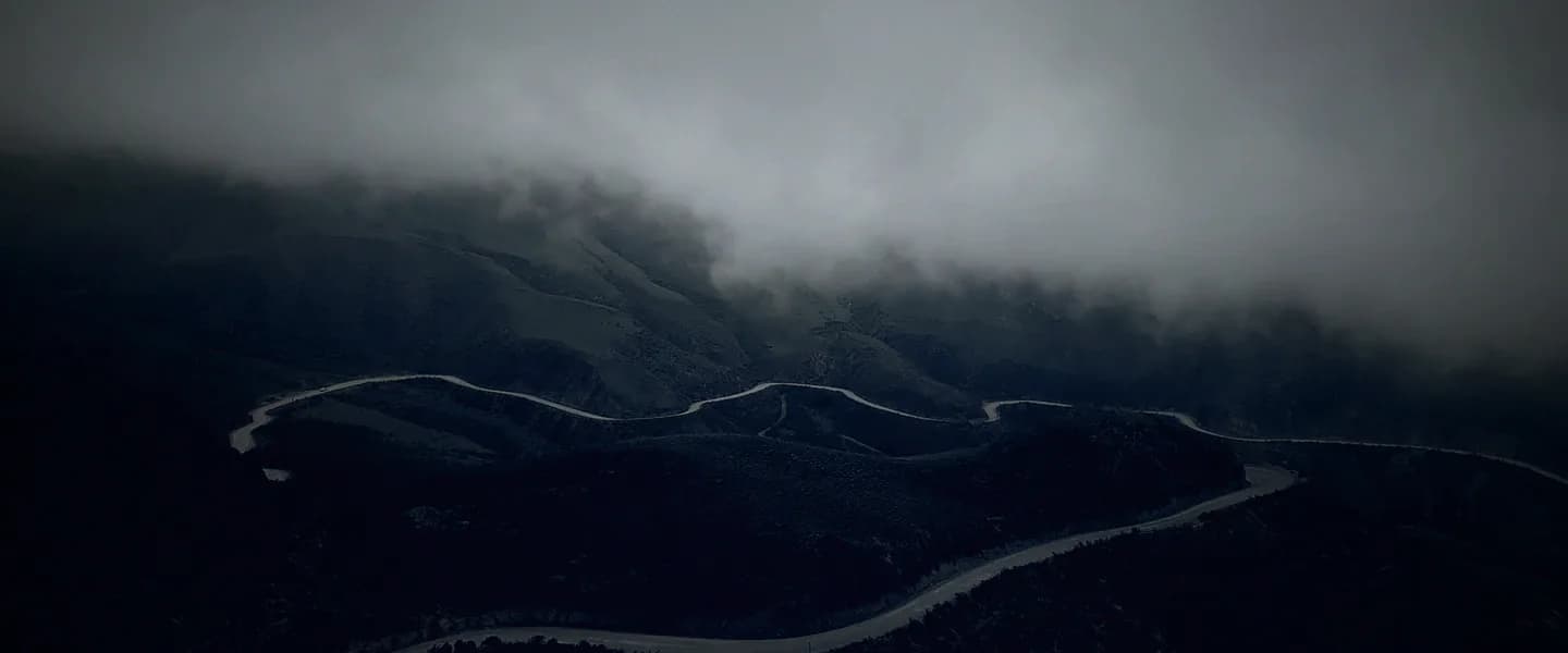 A winding road disappearing into the mountains under heavy cloud.