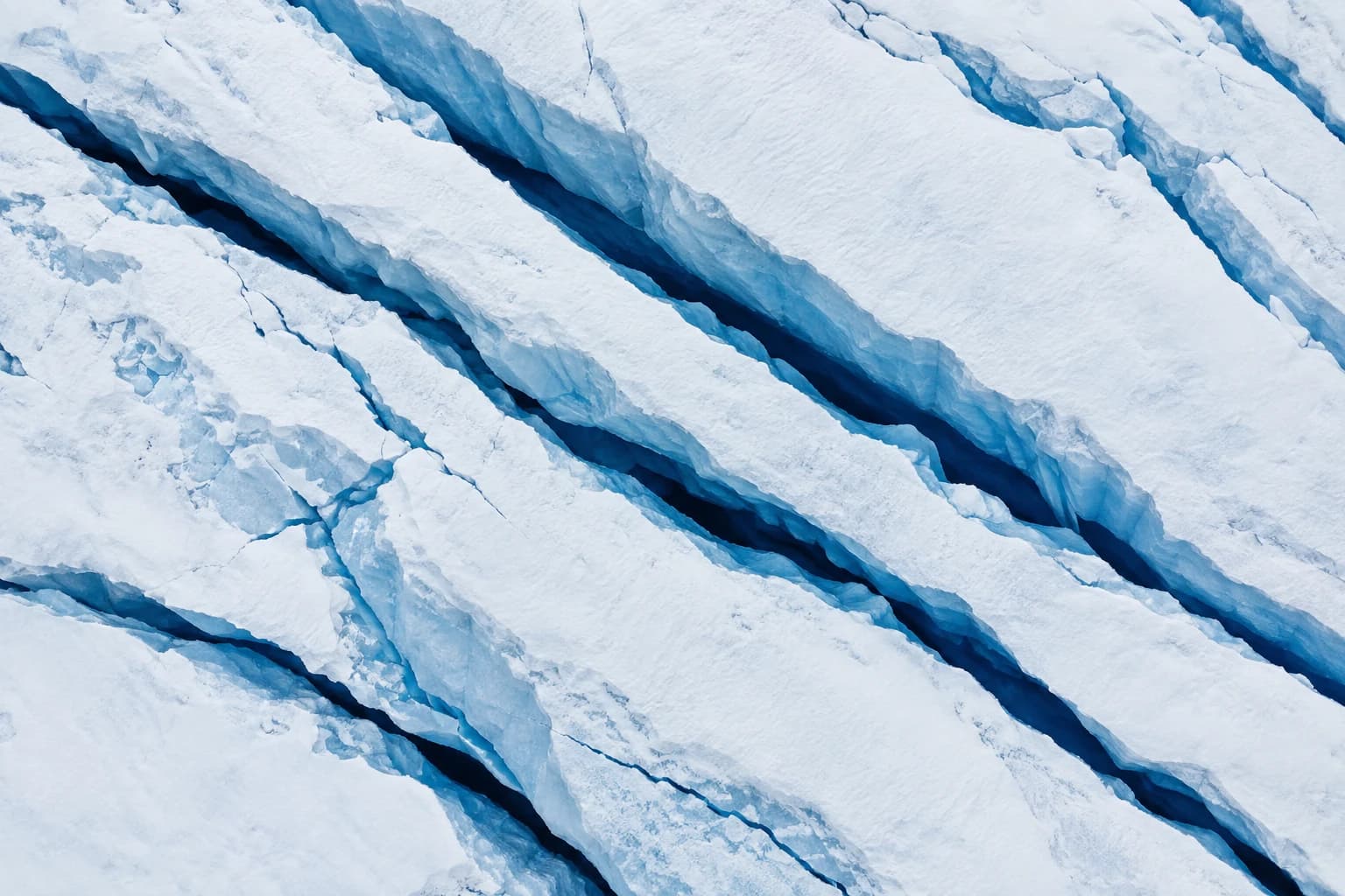 AI aerial photograph looking down on deep blue crevasses cutting across a white glacier.